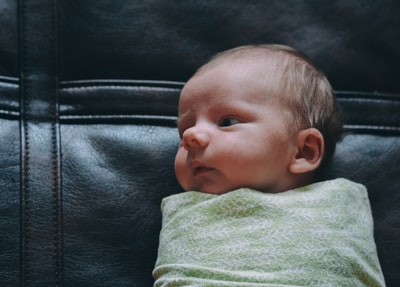 婴儿身上覆盖着黑色皮革表面的绿色毯子